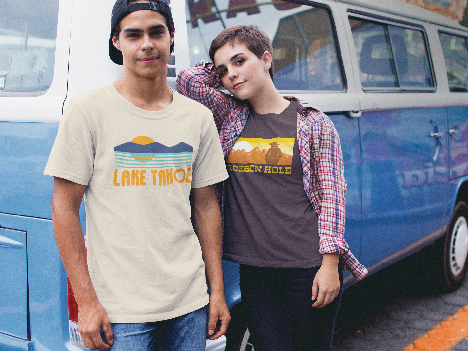 Two people, one wearing a Lake Tahoe t-shrit, the other wearing a Jackson Hole t-shirt with scenic designs in front of a blue van.